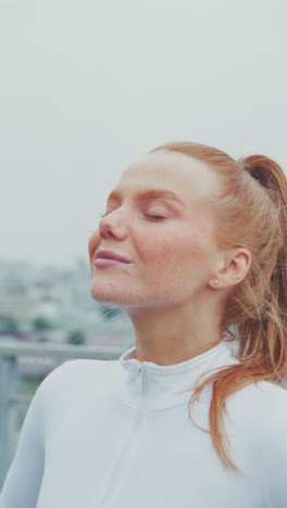a young woman in sportswear enjoys a moment of serenity and accomplishment outdoors amidst a cloudy urban landscape