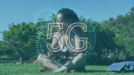 Animation-Des-Wortes-5g-über-Einer-Frau,-Die-Im-Park-Auf-Gras-Sitzt-Und-Ihr-Smartphone-Benutzt