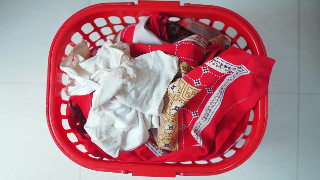 Person Placing Dirty White Clothing Into Red Laundry Basket
