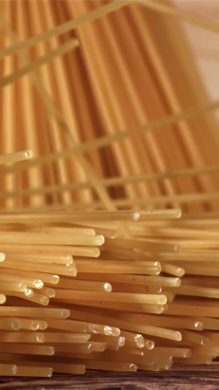 Spaghetti secchi che cadono su una superficie di legno al rallentatore