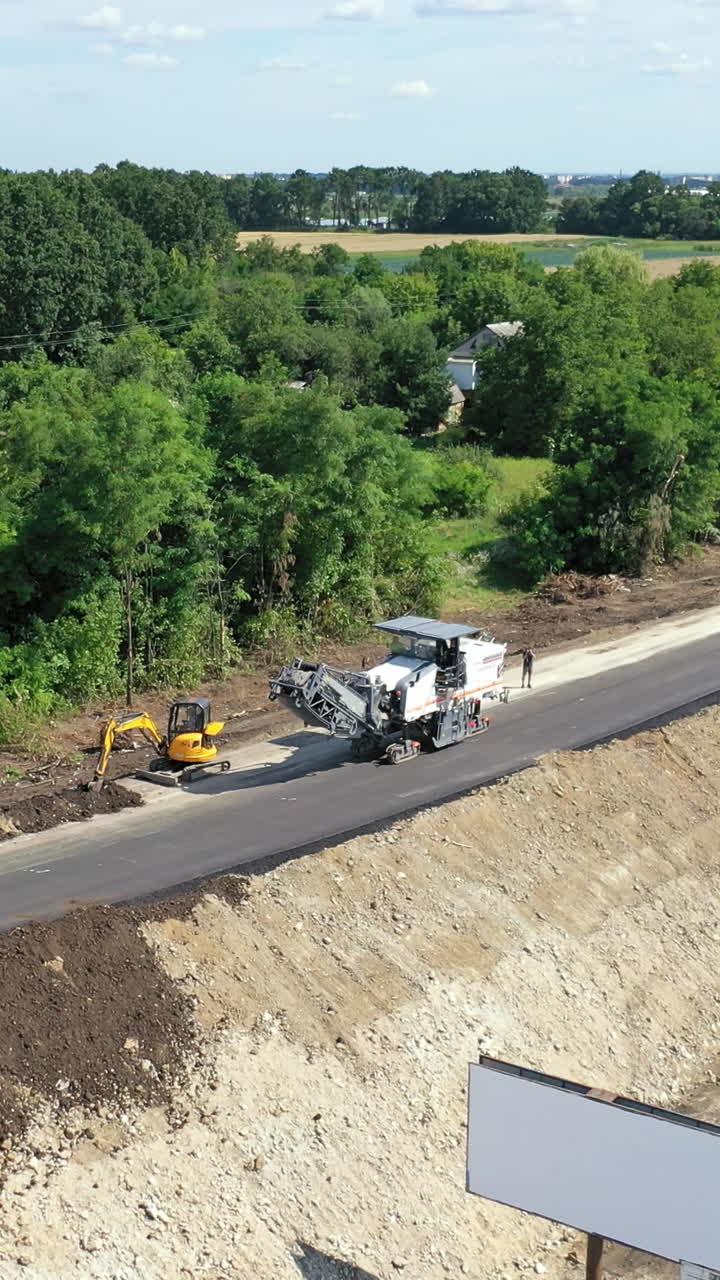 Roadworks of a new asphalt road. Modern machinery working on a road construction in summertime. Aerial view. Vertical video