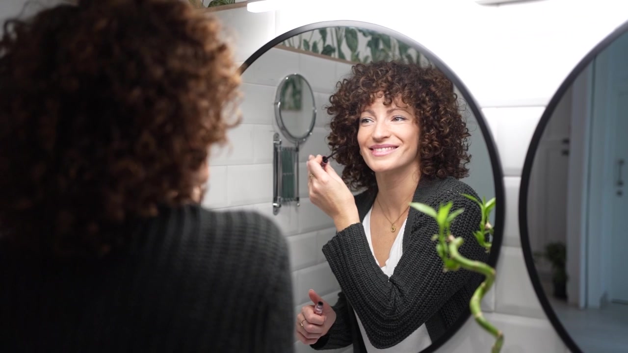 Una donna con bellissimi capelli ricci si trucca abilmente in un moderno bagno.