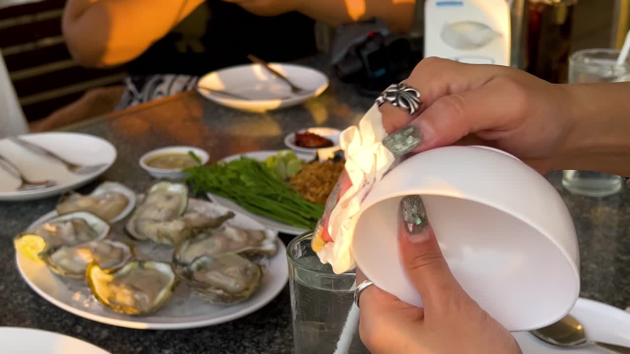Hands cleaning bowls and arranging oysters at a dining table with condiments and vegetables.