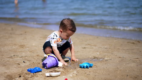 calm caucasian toddler squatted on the sea shore. focused kid plays with sand on sunny day.