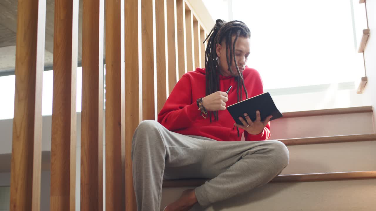 Un homme ajuste sa posture avant de taper sur une tablette avec un stylet et de faire défiler du contenu sur une marche d’escalier en bois