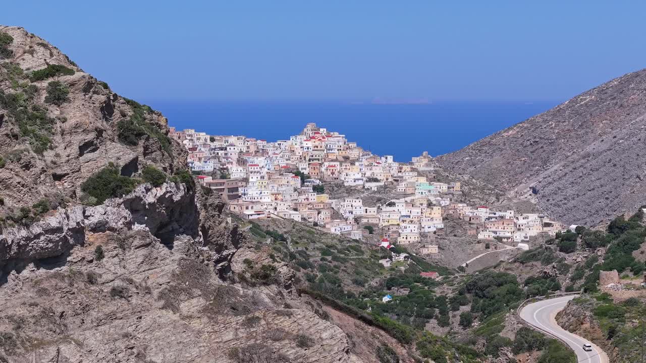 Drone footage capturing Olympos village of Karpathos as the drone gains altitude, revealing the colorful traditional settlement behind the hill with stunning Aegean scenery