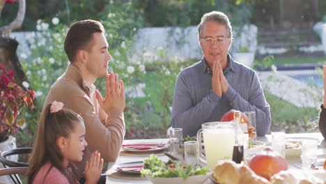 Video-of-happy-caucasian-parents,-daughter-and-grandparents-saying-grace-at-table-before-meal