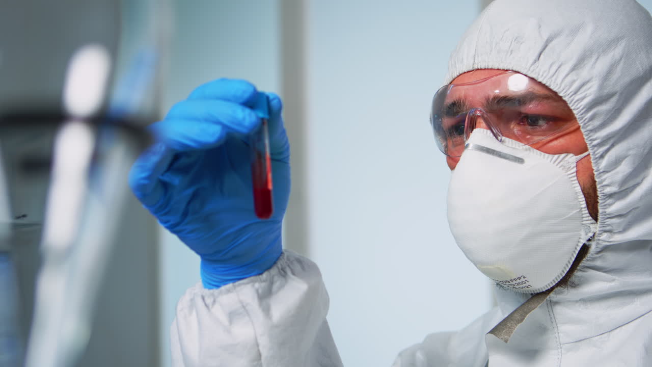 Científico con mono de trabajo examinando tubos de ensayo de sangre en laboratorio