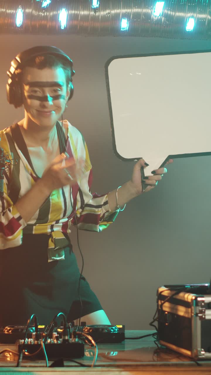 Video verticale. Una DJ tiene in mano un'icona a forma di fumetto in un locale notturno