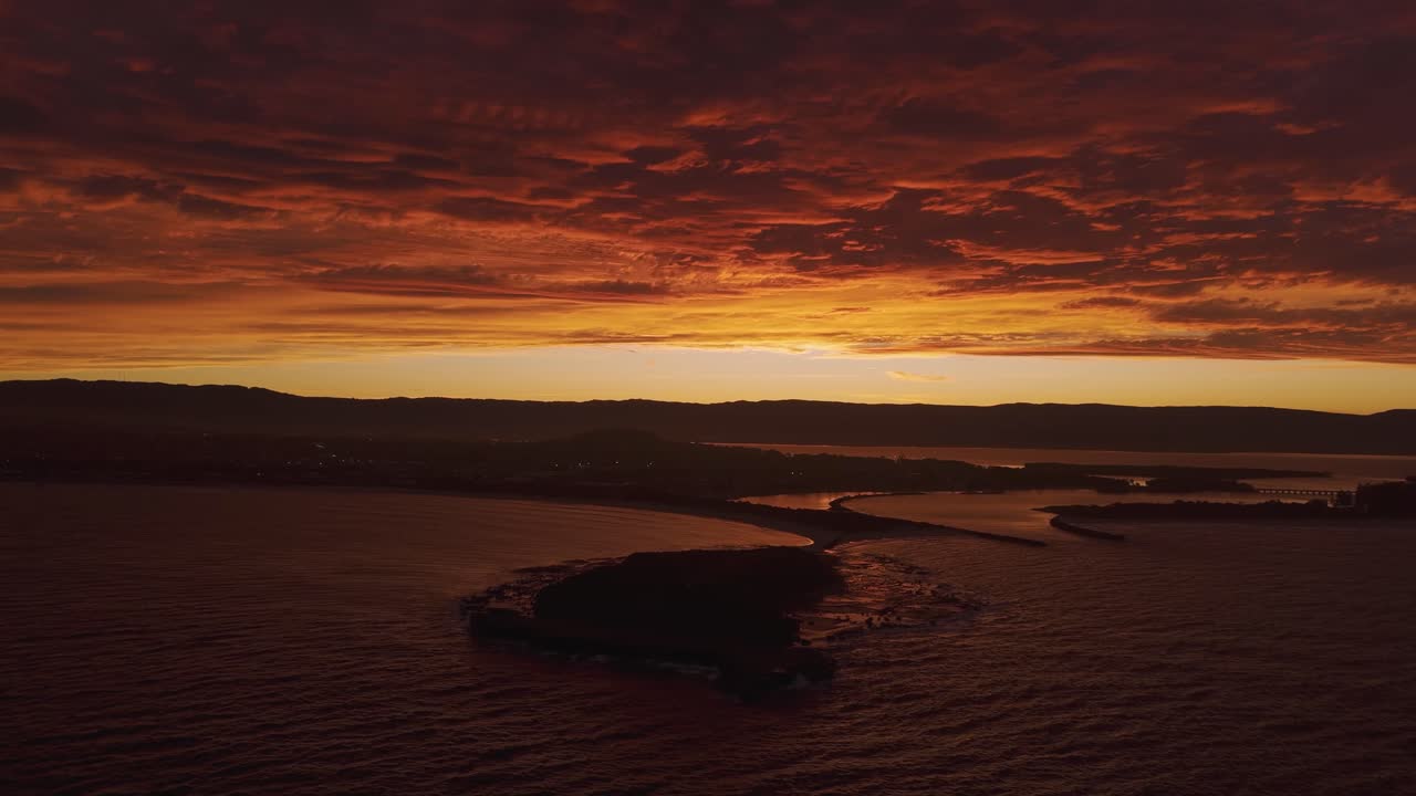 Atemberaubende Luftaufnahme von Windang Island, Australien, bei feuerrotem Sonnenuntergang, die den dramatischen Himmel und die ruhigen Gewässer hervorhebt