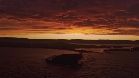 stunning aerial pullback of windang island, australia at fire red sunset, highlighting the dramatic sky and tranquil waters