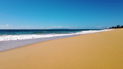 4K-Hawaii-Kauai-low-shot-trucking-in-on-beach-along-ocean-waves-in-frame-left-washing-in-toward-bottom-of-frame-with-mostly-sunny-sky