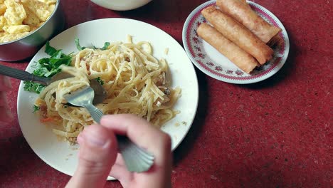 overhead view of eating a plate of pasta linguine with parmesan and basil served with lumpia or fried springrolls as side dish