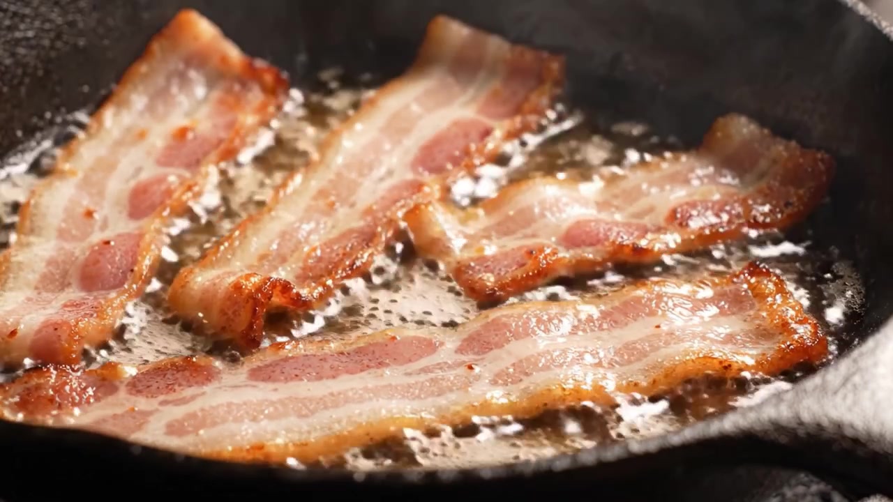 Bacon sfrigolante in una padella di ghisa: un viaggio visivo che fa venire l'acquolina in bocca, di croccante perfezione e una cottura ricca di sapore in ogni inquadratura.