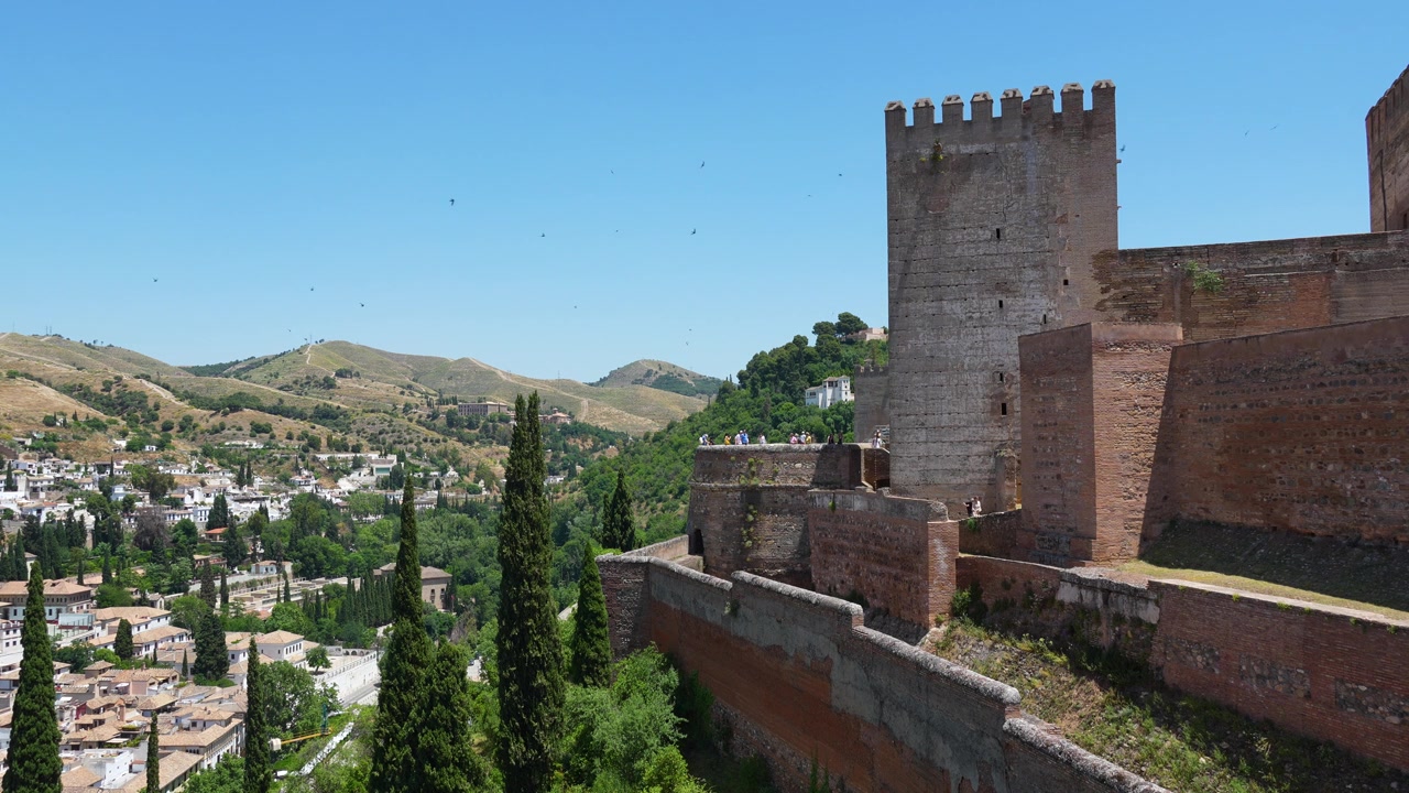 Torre histórica e muralhas defensivas da fortaleza da Alcazaba no complexo da Alhambra, com vista para Granada, Espanha, e pássaros voando por cima