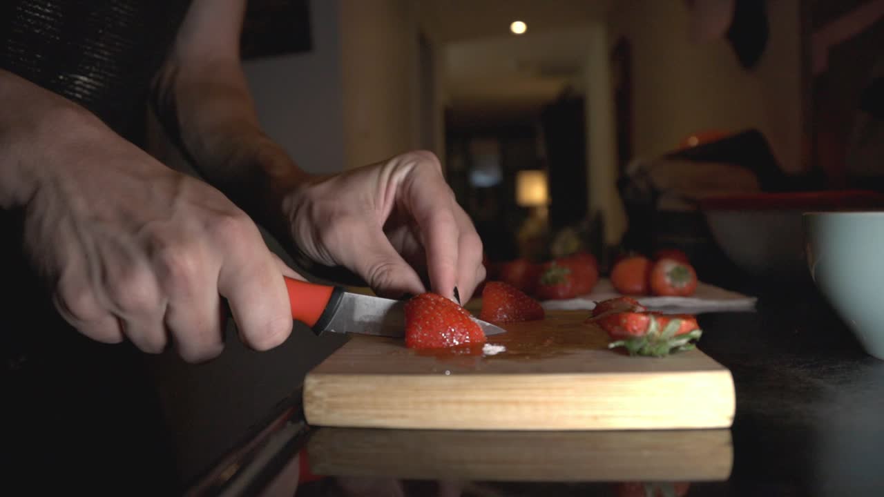 Person Cutting Strawberries On A Chopping Board And Putting It In A White Bowl. - close up shot