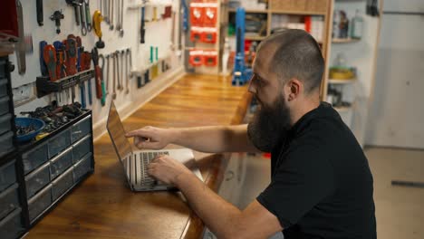 maestro caucásico usando computadora portátil en un taller de bicicletas