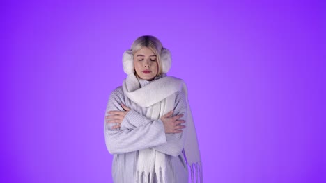 Blonde-Woman-Feeling-Cold-Rubbing-Hands-On-Sleeves,-Dressed-In-Winter-Clothes,-Purple-Background-Studio-Shot