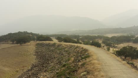 Slowly-rising-drone-aerial-showing-drought-and-smokey-conditions-in-summer,-smoke-hangs-in-the-air-covering-the-landscape-with-hills-barely-visible-in-the-distance