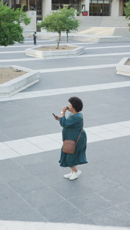 vertical video of plus size biracial woman walking on street with smartphone