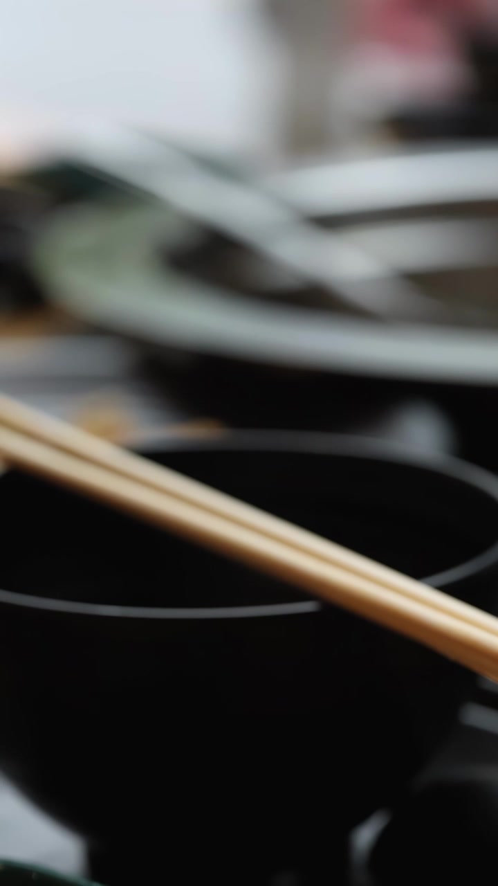 Lenta panoramica su un'elegante tavola apparecchiata per hotpot con bacchette, ciotole nere e messa a fuoco ridotta