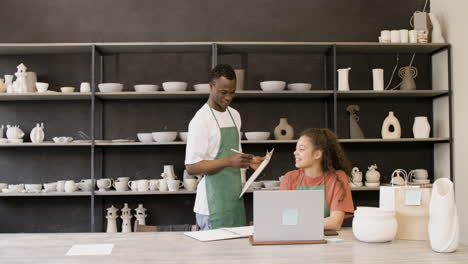 clerk holding a clipboard and talking with his female colleague in the pottery shop