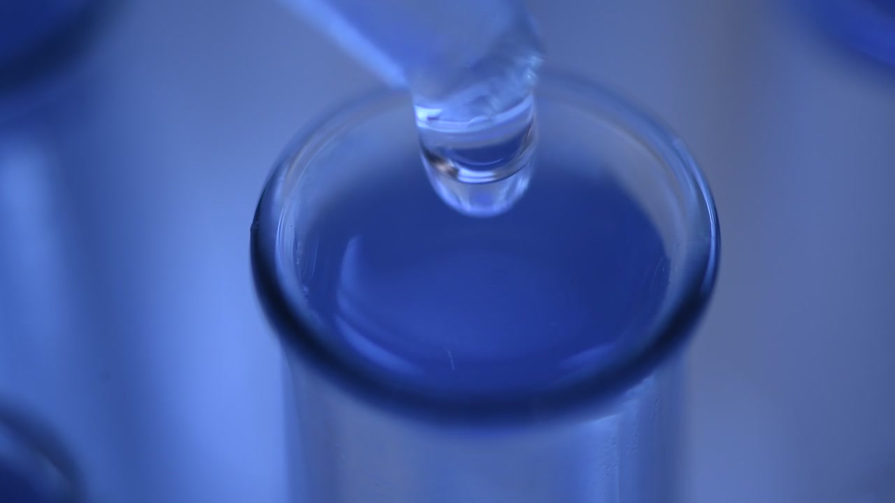 Primo piano di un contagocce che aggiunge liquido trasparente a una provetta blu