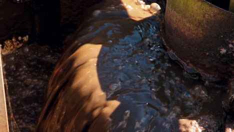 wastewater flowing over the edge of a treatment basin, showing dark liquid with a foamy, brown surface