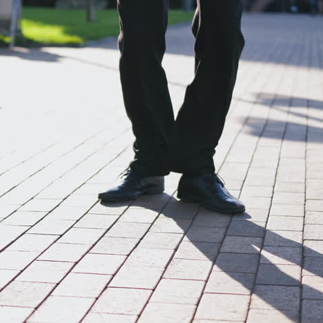 close-up for legs of man in black shoes dancing in the street. male's feet in black shoes and trousers dances happily on the pavement outdoors.
