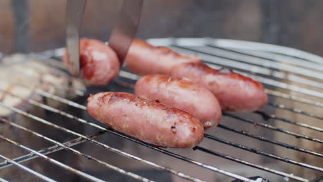 nahaufnahme einer nicht erkennbaren person, die würstchen auf dem grill dreht