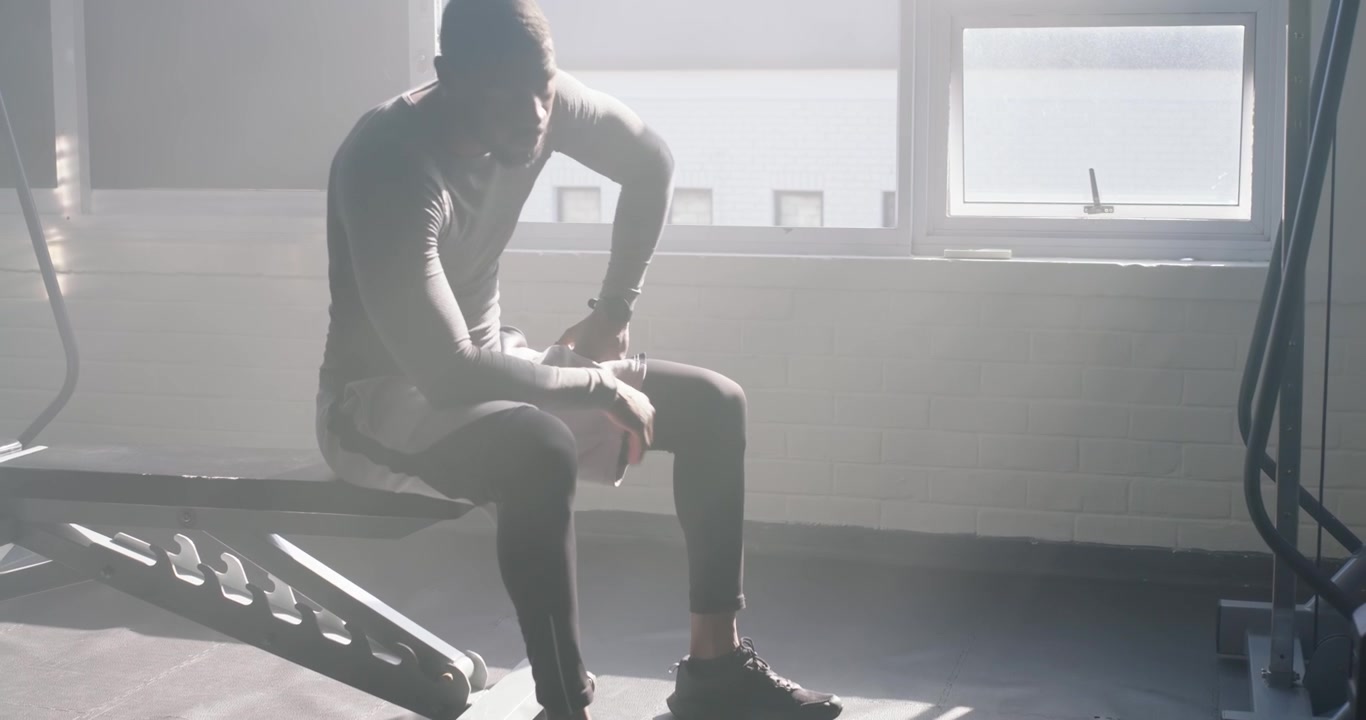 African man in athletic wear gripping rope performing triceps pulls training at gym checking watch