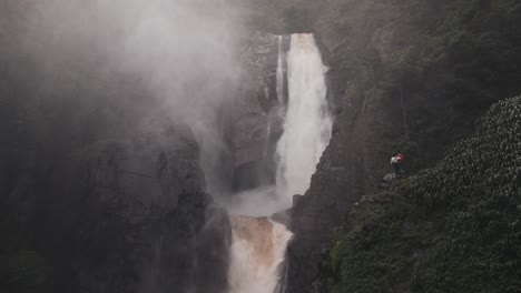 Tourist-Couple-On-The-Edge-Of-A-Cliff-Enjoying-Scenic-View-Of-Salto-de-Bordones-In-Huila,-Colombia---drone-shot