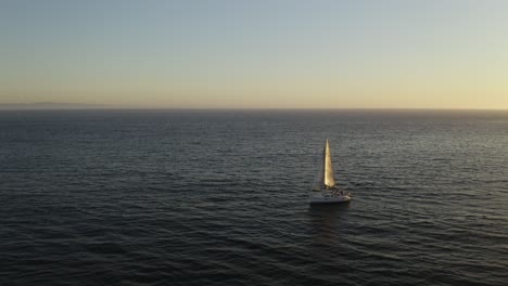 drone reveals yacht blowing in wind alone at sea, sunset on ocean