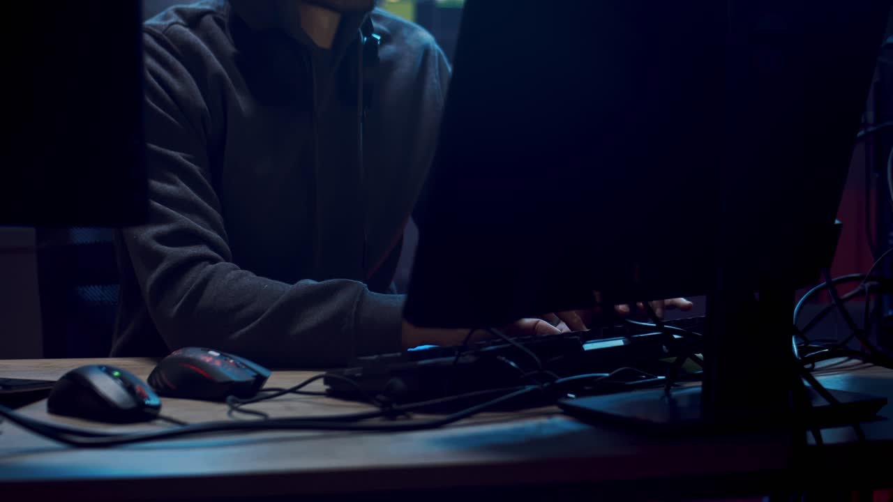 Male Software Developer And Programmer In A Hood Working At Night At The Two Big Screen Of Computers In The Dark Room With Technologies