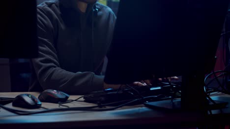 male software developer and programmer in a hood working at night at the two big screen of computers in the dark room with technologies