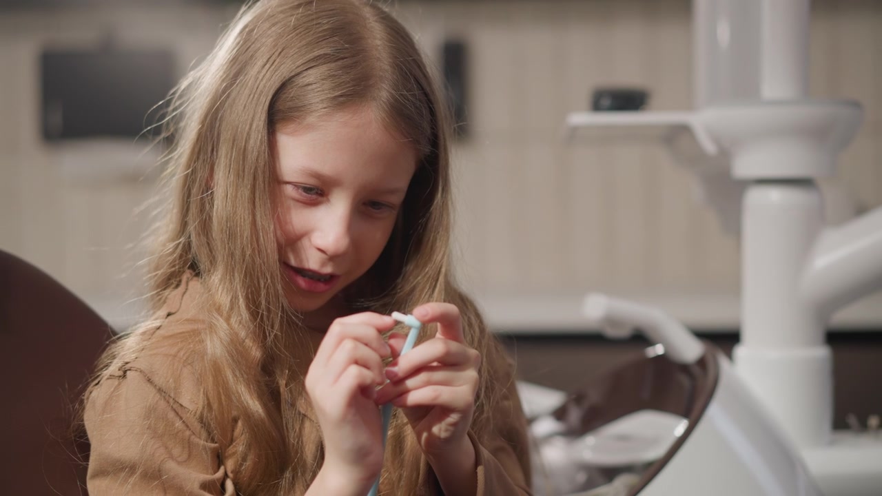 Close up of young girl holding dental floss in orthodontic clinic setting. Girl appears to be preparing for or following teeth cleaning procedure with professional equipment visible