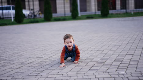 funny little kid crawling by the paved ground outdoors. cute toddler approaching the camera.