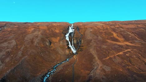 waterfall in iceland cascading down a steep mountain in autumn - aerial parallax