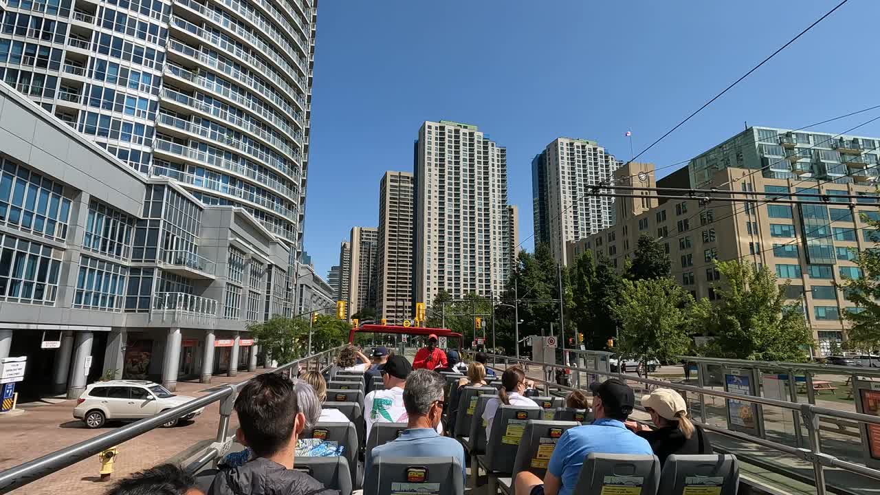 First-person view of Passengers on open-top bus tour through Toronto, surrounded by modern high-rise buildings and vibrant city life. Urban architecture and street atmosphere downtown Toronto, Canada