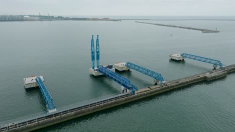 vista aérea de las grúas portuarias y los muelles de carga vacíos en el puerto de liepaja, la ciudad de liepaja en el fondo, día de verano nublado, amplia toma de avión no tripulado avanzando, inclinándose hacia abajo