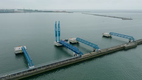 aerial establishing view of port cranes and empty loading docks at port of liepaja , liepaja city in the background, overcast summer day, wide drone shot moving forward, tilt down