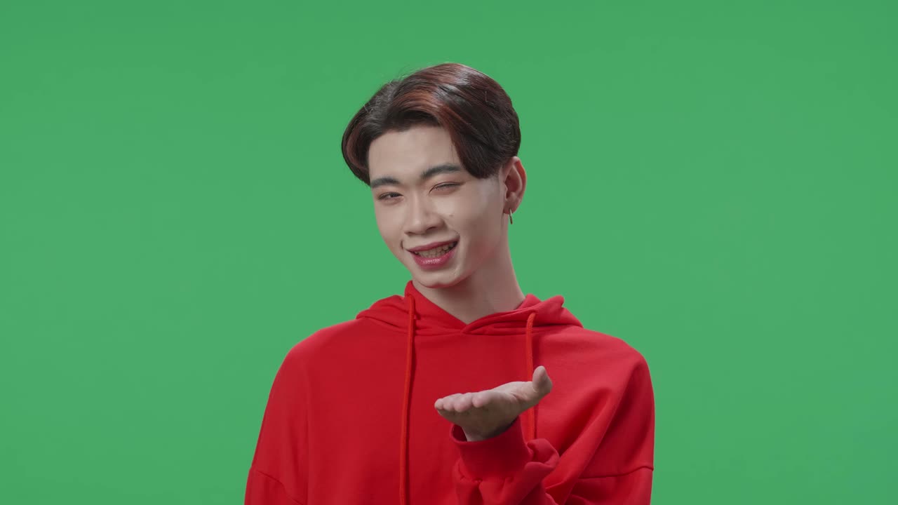 A Portrait Of A Smiling Asian Transgender Male Blowing Kisses To A Camera In The Green Screen Studio