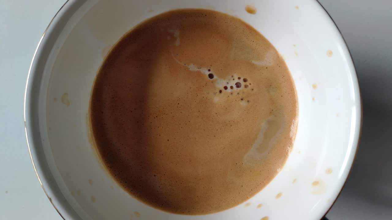 A cup of coffee being poured with milk, showing a smooth texture and froth