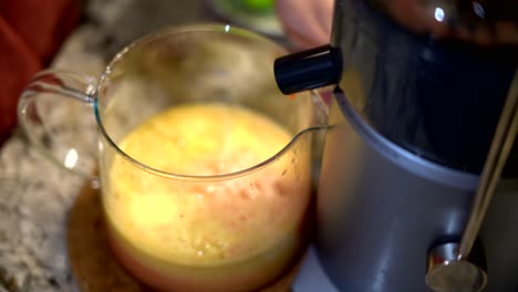 primer plano de la persona que usa exprimidor eléctrico con boquilla vertiendo jugo de fruta saludable en una jarra de vidrio - aparato de cocina exprimidor eléctrico que hace jugo de fruta fresca saludable enfoque selectivo primer plano