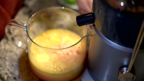 close up of person using electric juicer with nozzle pouring healthy fruit juice into glass pitcher - electric juicer kitchen appliance making healthy fresh fruit juice selective focus close-up