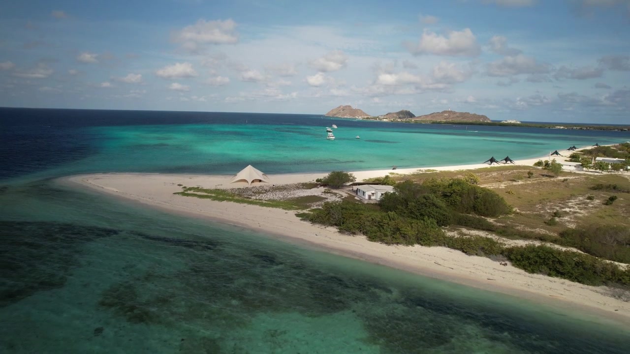 Spiaggia incontaminata di Isla Madrisky e acque turchesi caraibiche sotto un cielo soleggiato, vista aerea.
