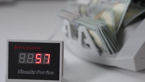 display with figures of cash counter machine. one hundred dollar bills falling on the holder of money counting equipment. close up. blurred backdrop.