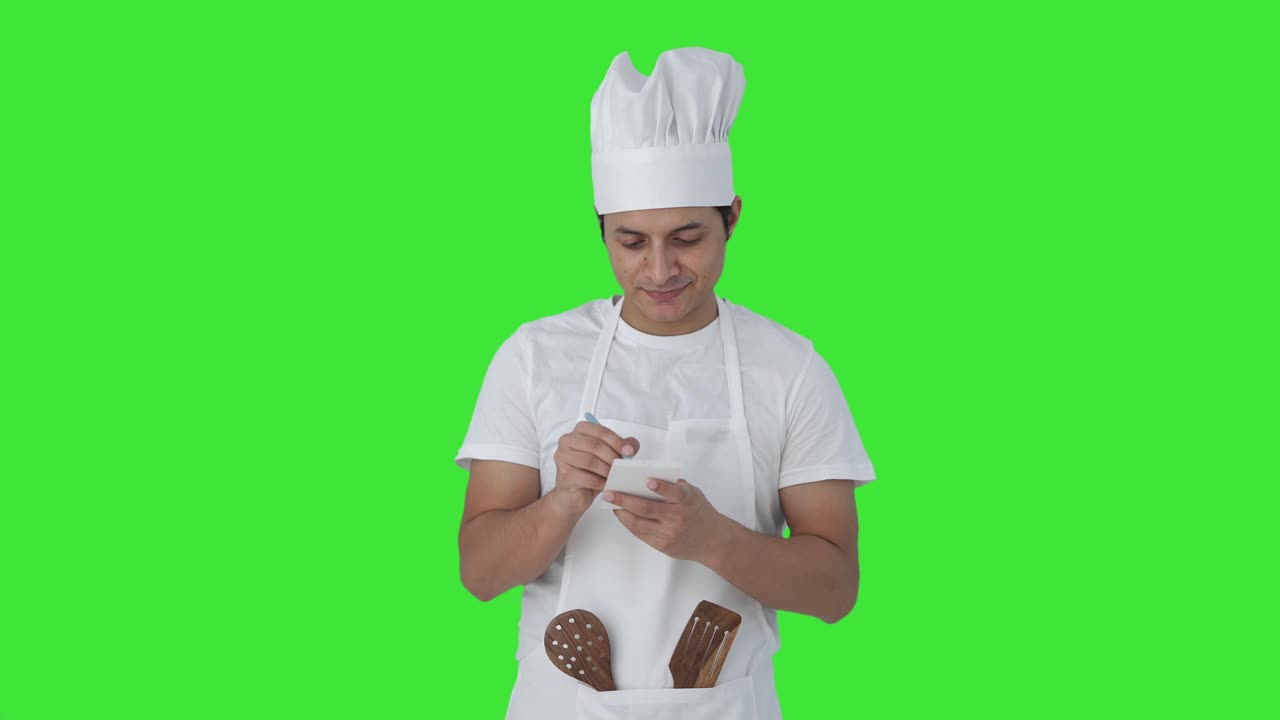 Chef professionista indiano felice che annota una ricetta, schermo verde
