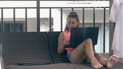 woman-with-ponytail-lies-on-lounger-and-works-on-laptop