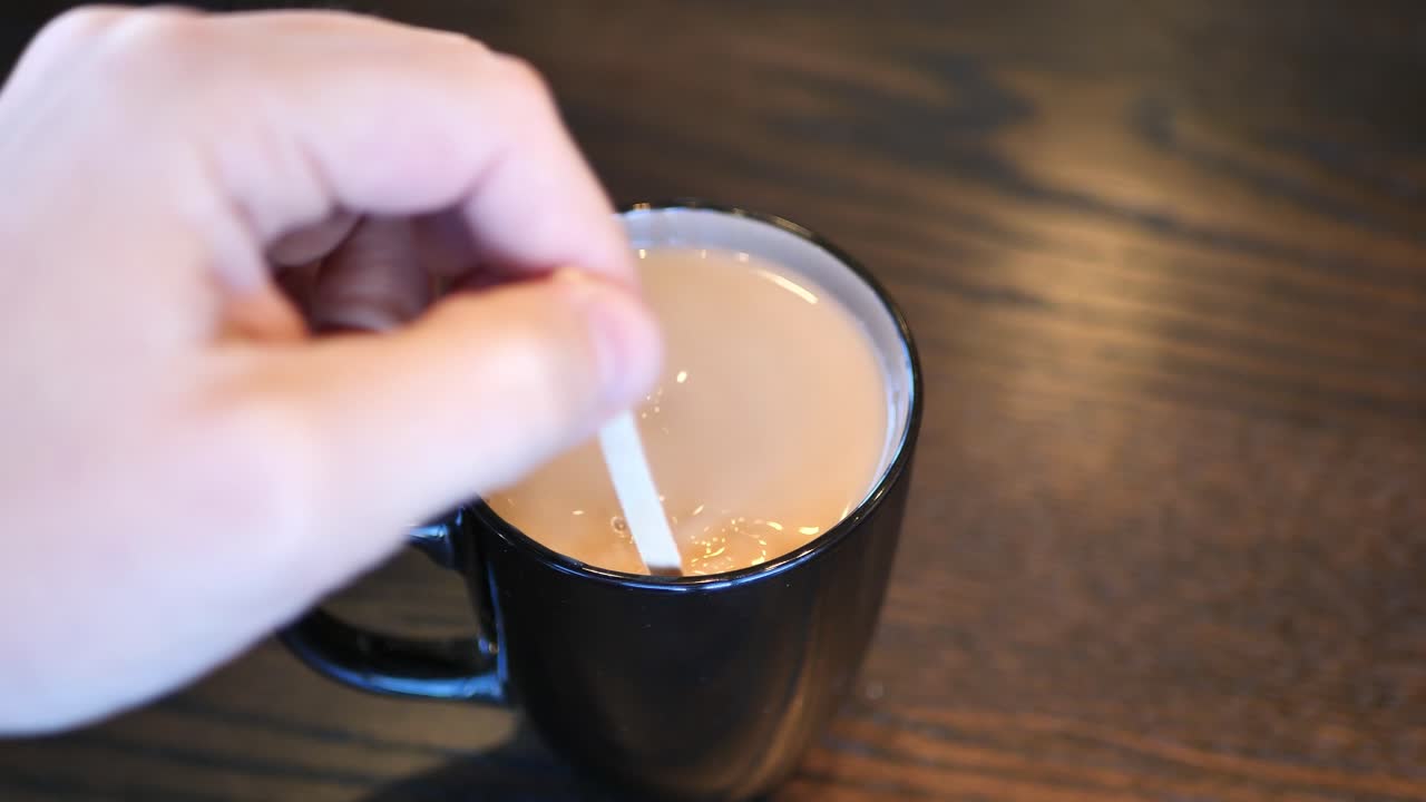 Clip taken at coffee shop cafe of a caucasian man stirring a black and brown coffee cup with hot coffee or tea in it